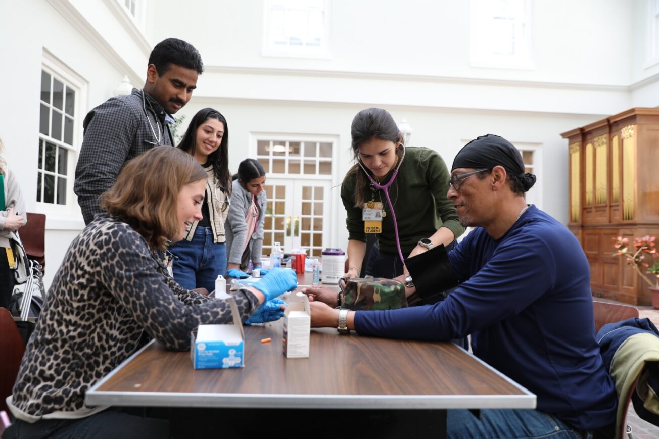 Student Family Medicine Association members (clockwise from left) Lana Sumner-Borema, Krishal Somasundaran, Samara Shabon and Mariana Fernandes Gragnani check the blood glucose levels of a downtown community member (Photo by Arda Athman, School of Medicine)
