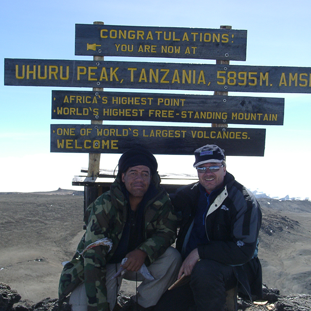 two men in front of sign on top of Mt. Kilimanjaro