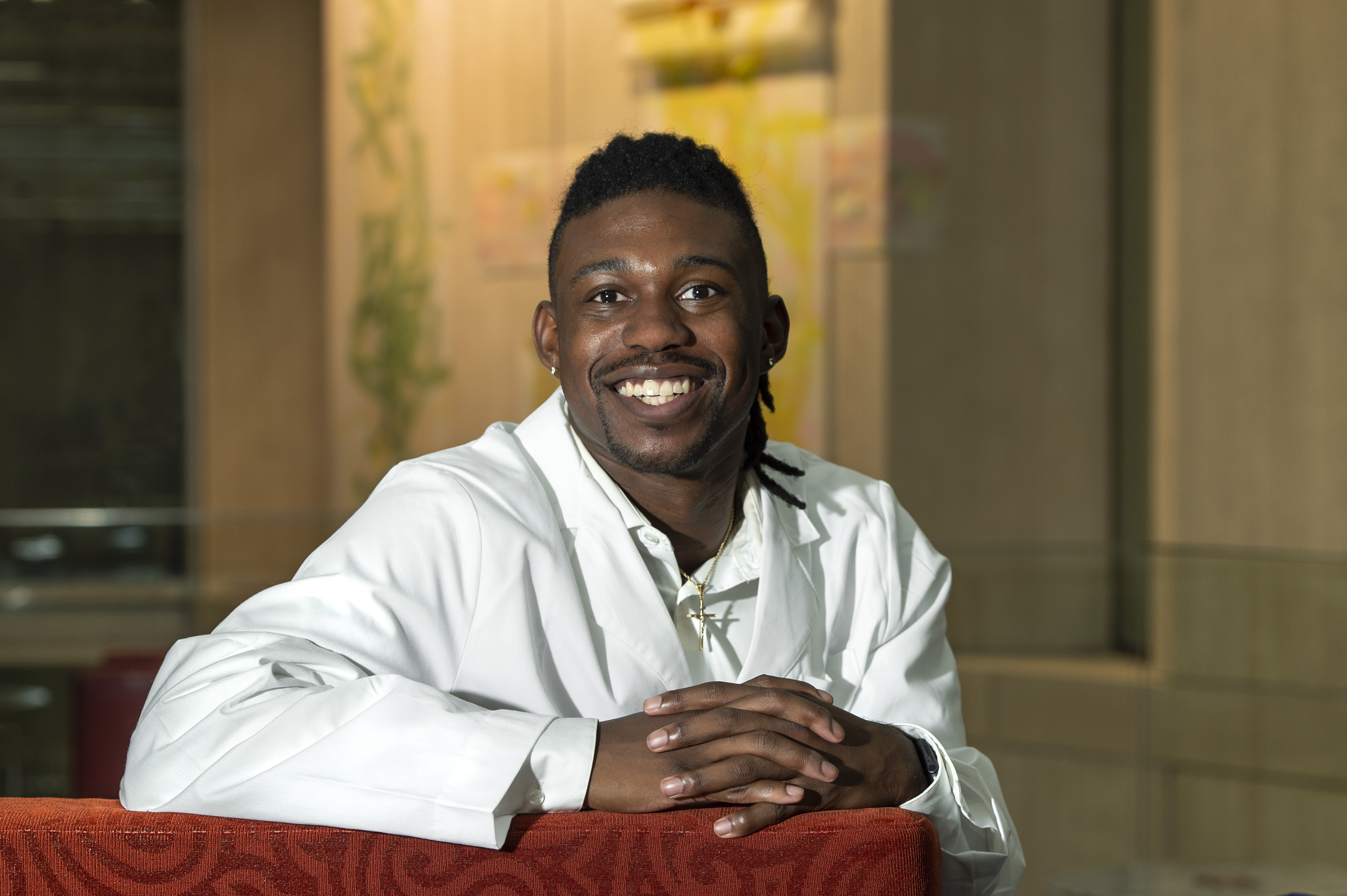 The Class of 2025's Gabe Thomas smiling and wearing a white coat sitting in a red chair in McGlothlin Medical Education Center