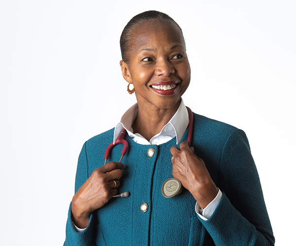 Alice Coombs standing in front of a white background, smiling and holding a stethoscope around her neck