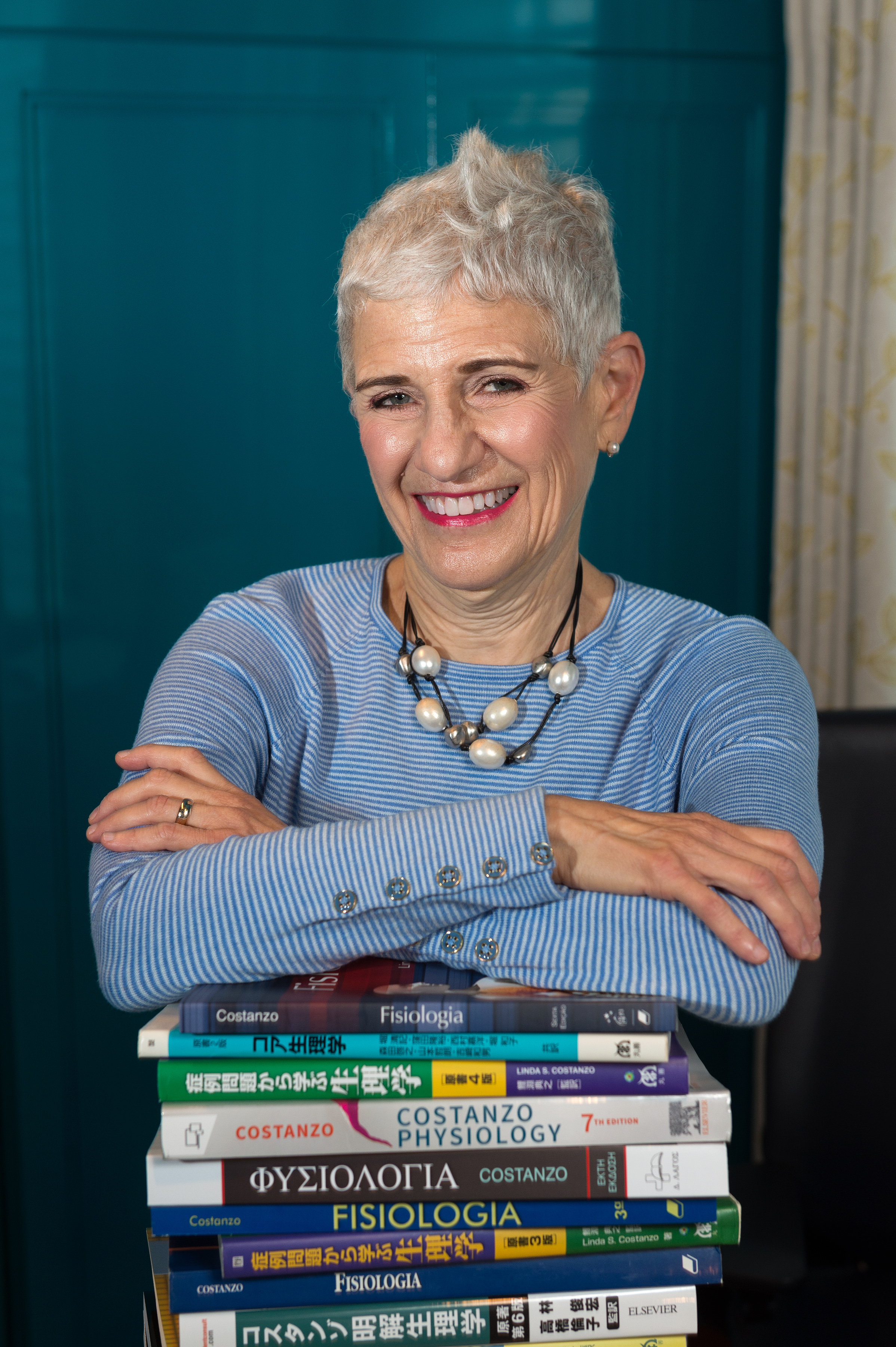 Linda Costanzo PHD leaning over a stack of books