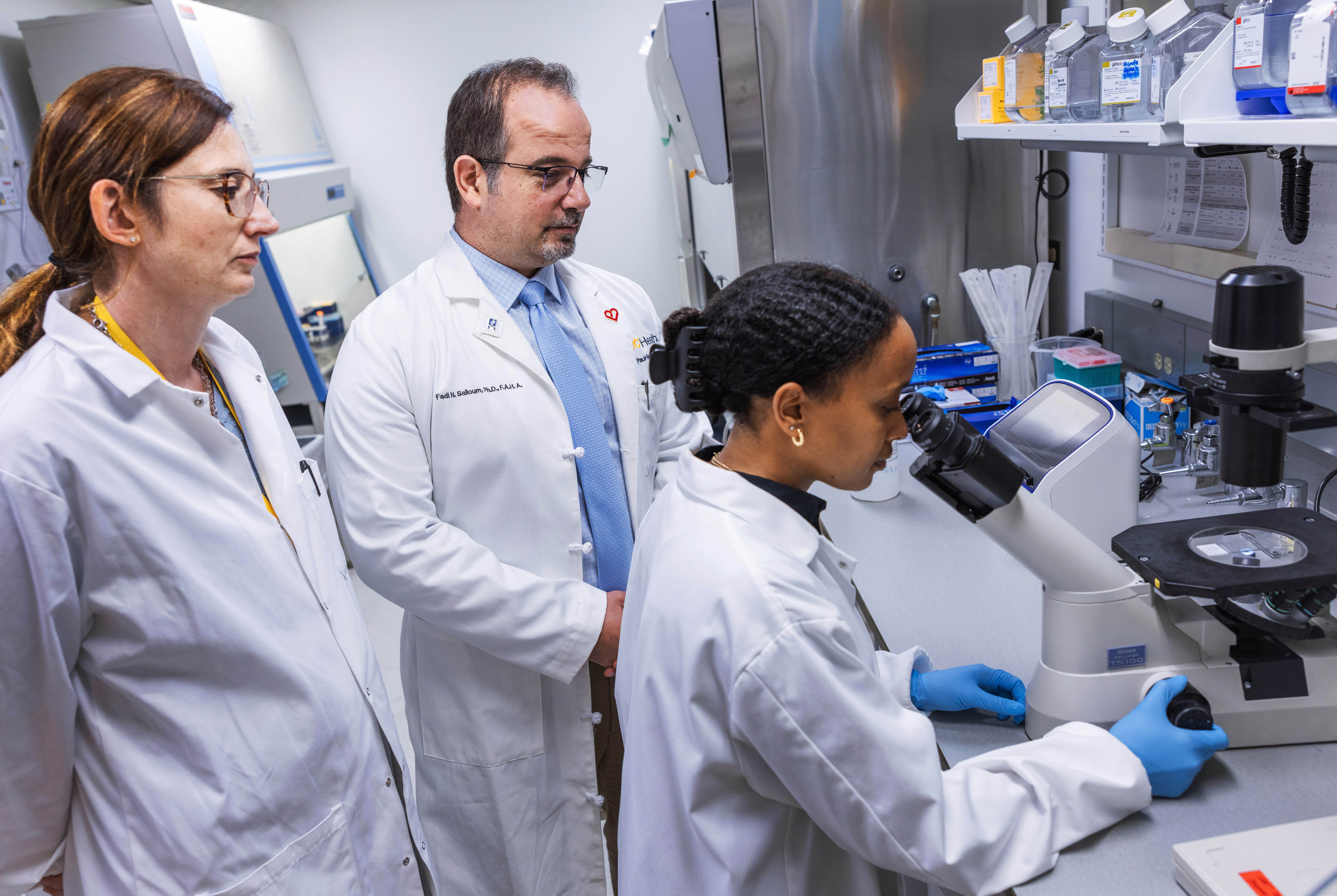 Senior lab and research manager Eleonora Mezzaroma, Ph.D., and Salloum work with Nigeste Carter, a fifth-year doctoral candidate in the Department of Pharmacology and Toxicology, as she looks through a microscope.