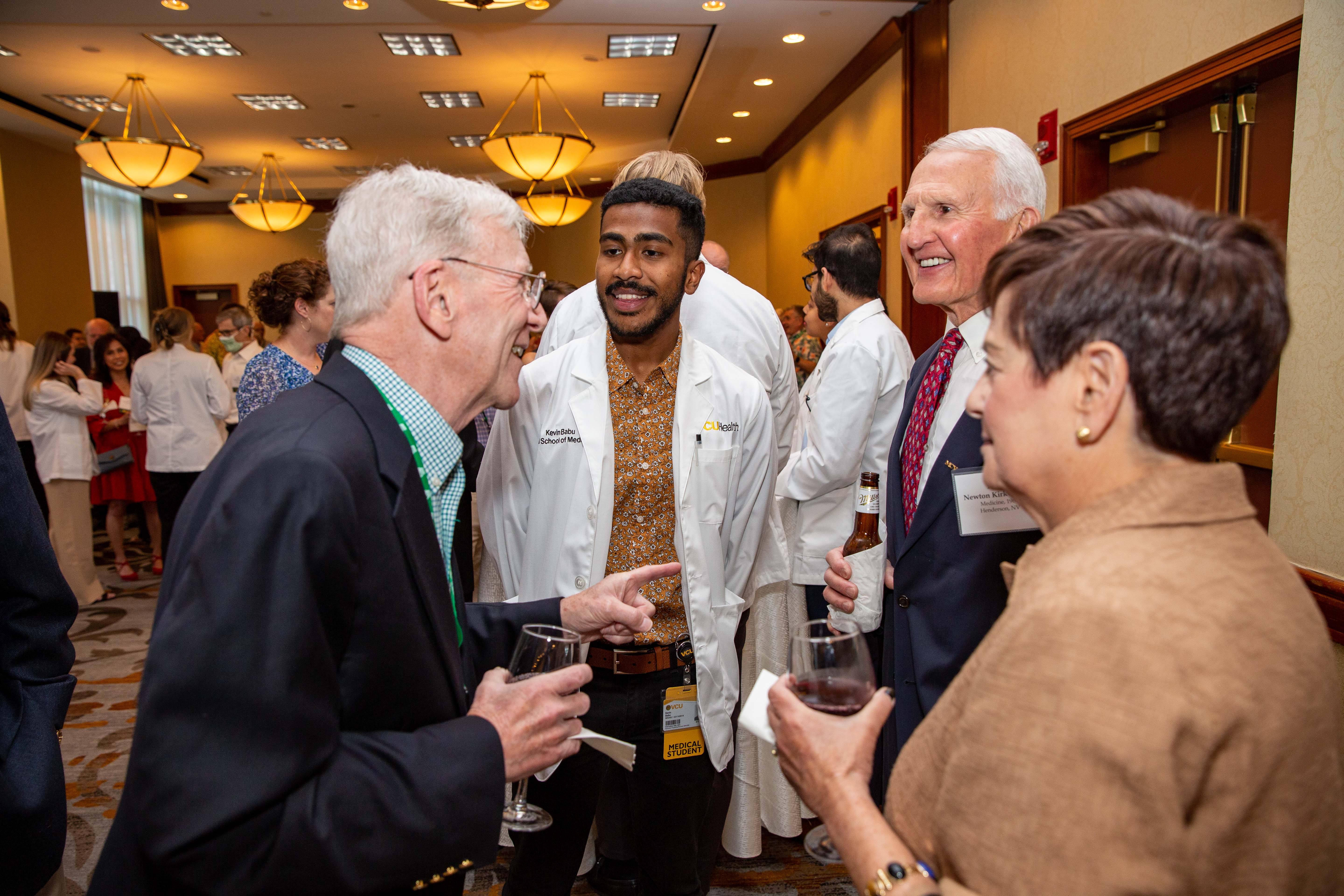  Alumni smile and talk with a medical student wearing a white coat 