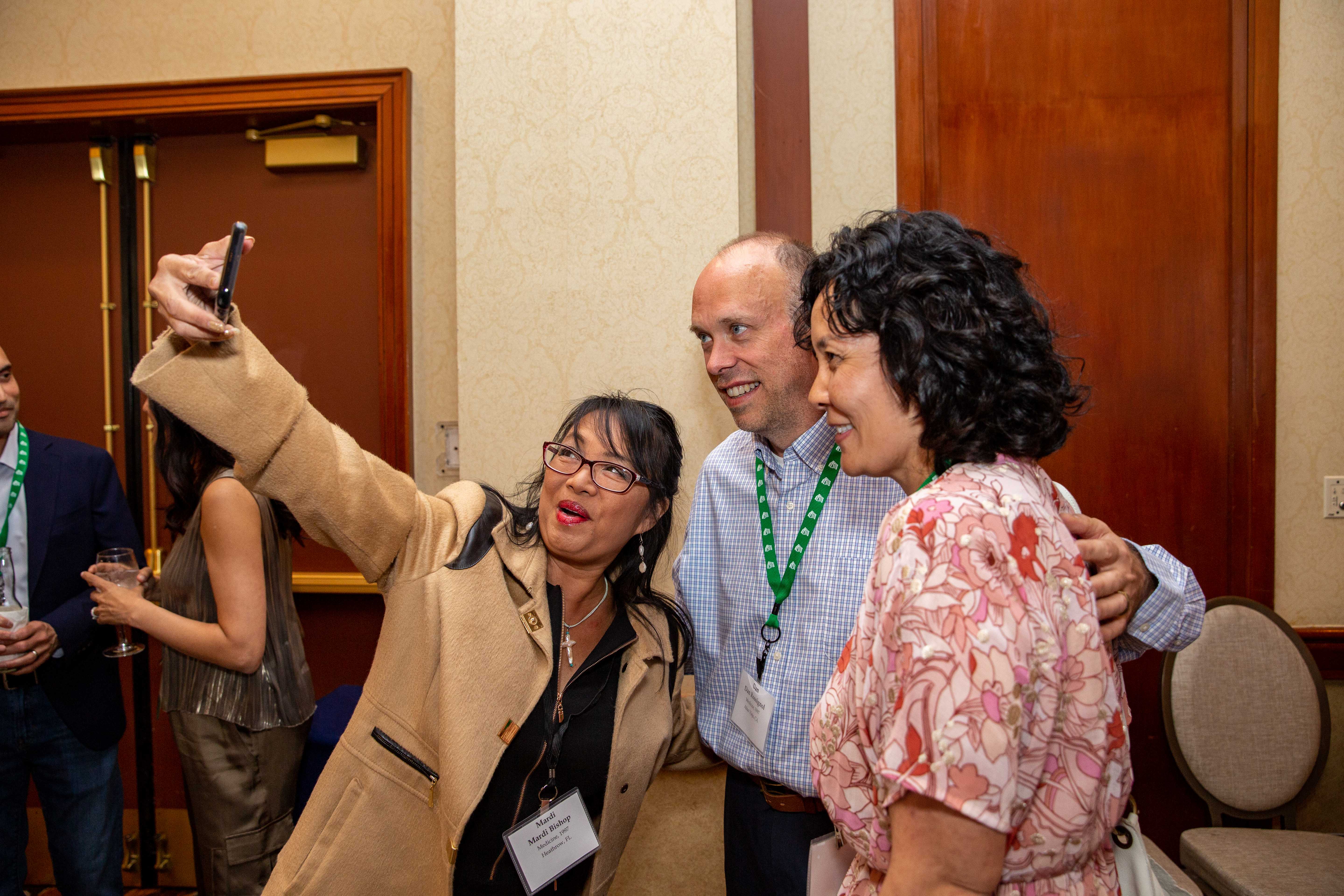 Three alumni hold up their phone and take a selfie