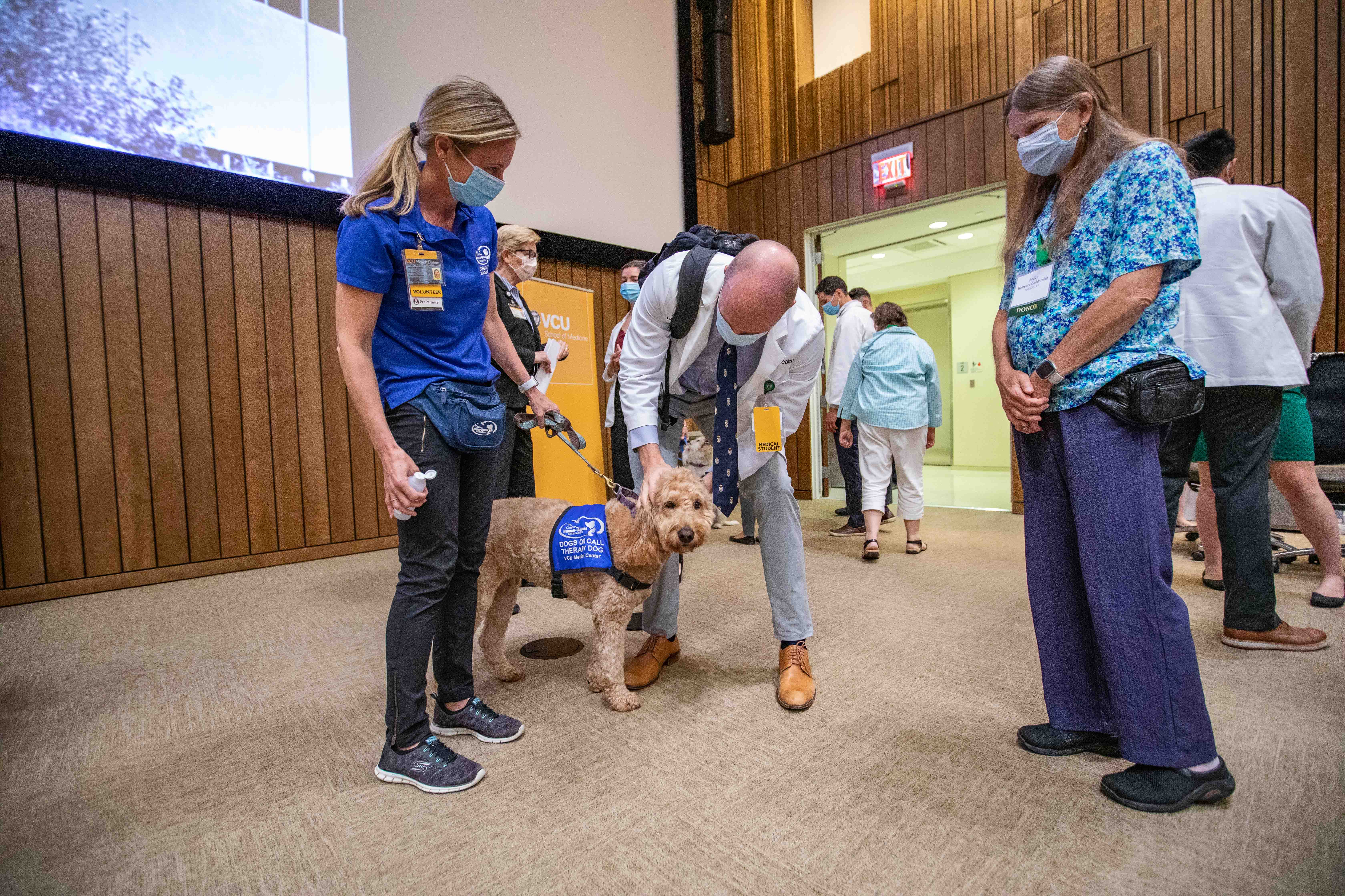  Student pets Dog on Call while handler and alum look on 