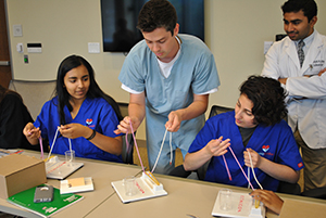 Camp organizer Ameya Chumble watches cardiology fellow Ryan Melchior, M.D., leads students through the surgical knots workshop.