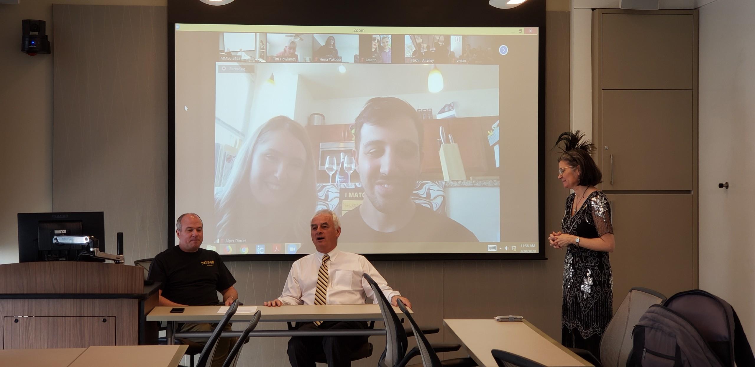 Class President Alper Dincer (pictured on video screen), Senior Associate Dean Chris Woleben, M’97 (on left), and Dean of Medicine Peter Buckley, M.D. (center),