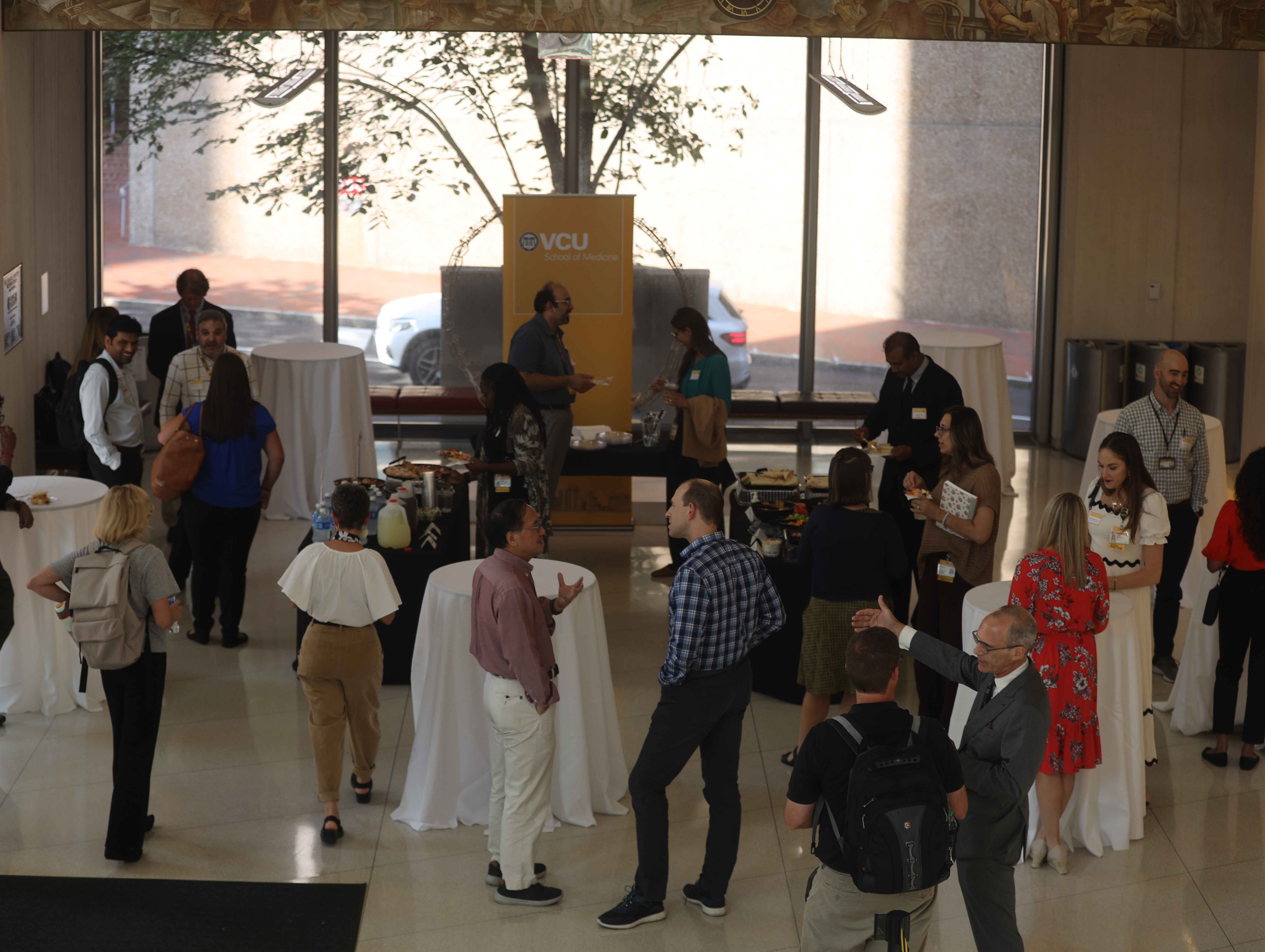 group of people standing in a lobby talking to each other and eating